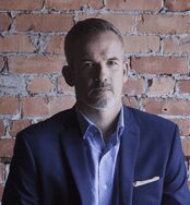 A man in a suit and tie standing next to a brick wall.