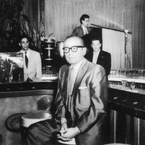 A man in glasses and suit sitting at a bar.