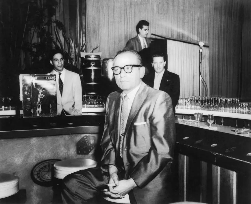 A man in glasses and suit sitting at a bar.