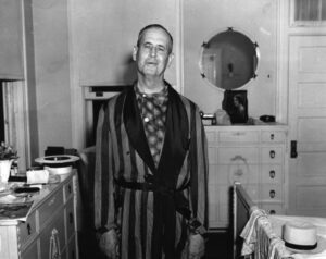 A man in striped robe standing next to dresser.