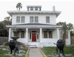A white house with two black dogs statues in front of it.