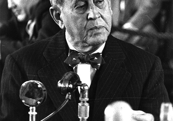 A man in a suit and bow tie is sitting at a microphone.