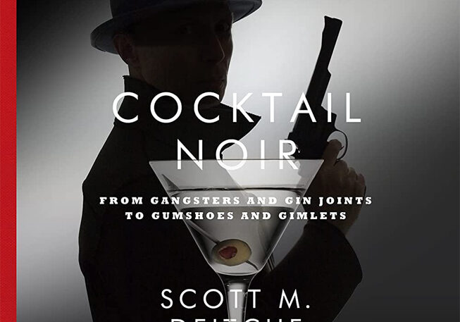 A man holding a gun in front of a martini glass.